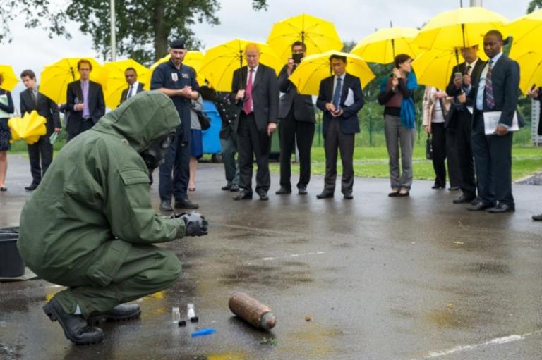 Militairen van DOVO demonstreren, tijdens een fikse regenbui, hoe ze chemische munitie identificeren en klaarmaken voor vervoer.